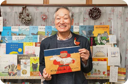 店主がおすすめの絵本を手に笑顔で紹介している様子